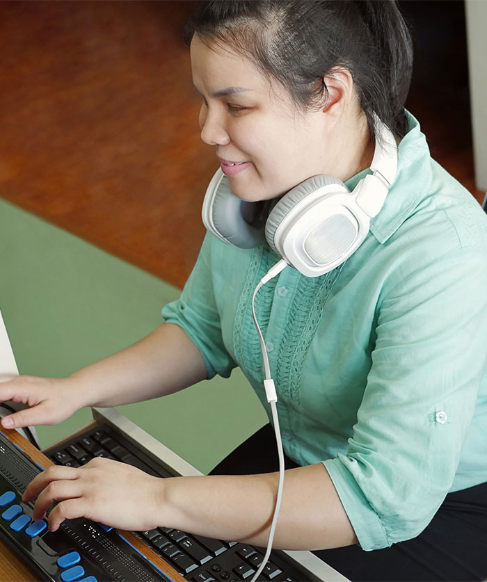 Photo of a woman with headphones using an assistive keyboard for blind users.